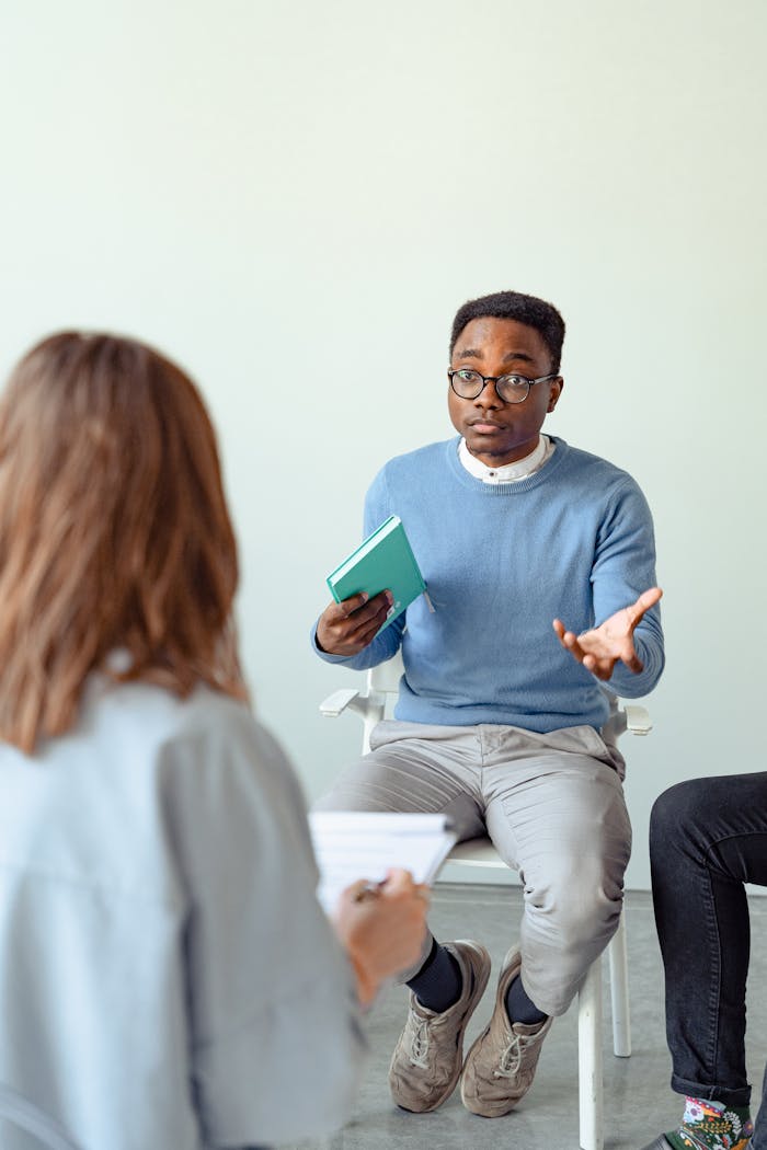 Male therapist engaging clients during a therapy session indoors, promoting mental health awareness.