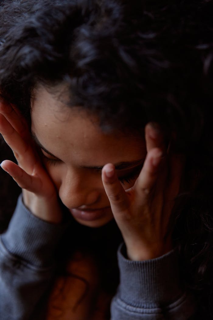 Close-up portrait of a woman with hands on face expressing deep thought and emotion indoors.